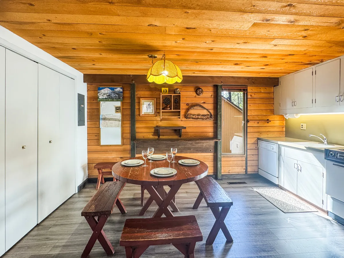 A view of the spacious wooden dining table set amid warm paneling with a glimpse of the kitchen area in the background. The setup is perfect for shared meals, celebrations, and family gatherings, all within the heart of the open living space.