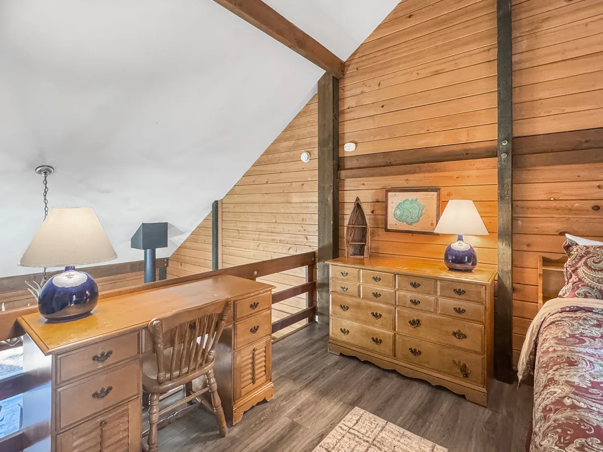 A tranquil bedroom scene with exposed wooden beams, a cozy bed, a dresser, and a desk with a reading lamp. Personal touches like an open book and soft bedding create an inviting atmosphere for unwinding after outdoor adventures.