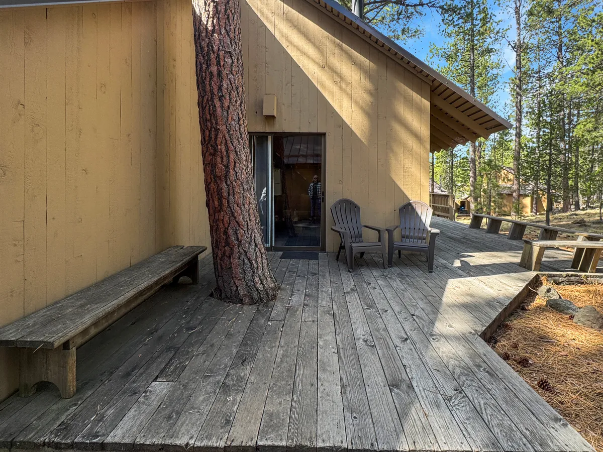 A wooden deck bordered by trees, featuring adirondack chairs that face into the forest. The deck is bathed in soft sunlight, inviting families to relax, read, or gather together after a day of activity.